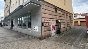 A multi-story building with a ground-level commercial space, a covered entrance, and a brick-paved street. - Cozy attic apartment main station/city (Nürnberg)