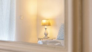 A room with a bedside lamp, a patterned pillow, and a white bedspread. - Bardolino Golden Hill (Bardolino)