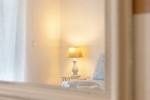Ein Zimmer mit einer Nachttischlampe, einem gemusterten Kissen und einer weißen Bettdecke.