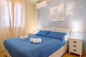 Ein Schlafzimmer mit einem Bett, zwei Nachttischen, einer Wand-Klimaanlage und einem Gemälde.