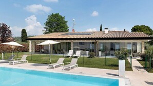 A pool with lounge chairs, a covered patio, and a house with a tiled roof. - Bardolino Golden Hill (Bardolino)