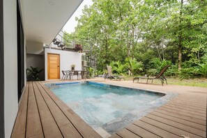 A modern outdoor pool area with a wooden deck, a small seating area, and lush greenery. - 4-bedroom Villa in Quepos close to Manuel Antonio w/Pool; A/C & TV in every room (Quepos)