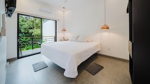 Un dormitorio con cama, mesita de noche, lámpara de pared, puerta corredera de vidrio a un balcón y un refrigerador negro.