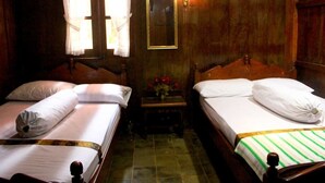A room with two beds, a wooden floor, a mirror, and a small table with flowers. - Joglo Mbah Guru Homestay (Ambarawa)