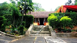 A stone staircase leading to a building with a tiled roof, surrounded by lush greenery and a red draped structure. - Joglo Mbah Guru Homestay (Ambarawa)