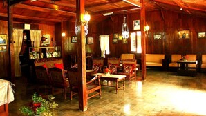 A wooden-floored room with a dining area, a sofa, and a table with a vase of flowers. - Joglo Mbah Guru Homestay (Ambarawa)