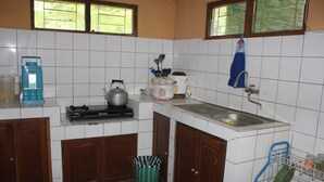 A compact kitchen with white tiles, a gas stove, a sink, and a window with blinds. - Joglo Mbah Guru Homestay (Ambarawa)
