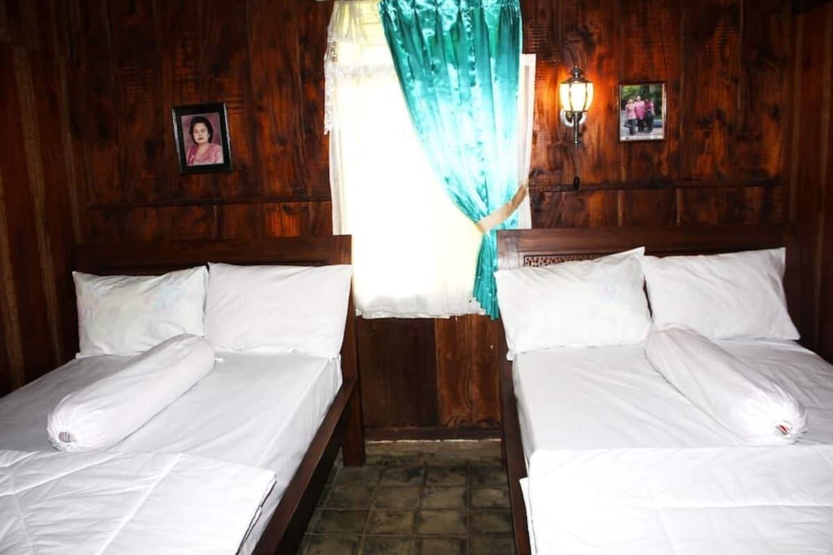 Quarto com duas camas de madeira, roupa de cama branca, uma cortina e duas luminárias fixadas na parede.