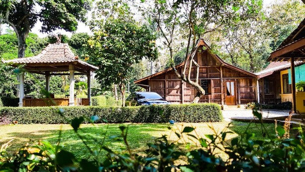 A traditional wooden house with a thatched roof, surrounded by a well-maintained garden and a gazebo. - Joglo Mbah Guru Homestay (Ambarawa)