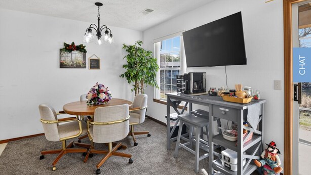 Et moderne kontor med et rundt bord, stole, en stor plante, et fjernsyn og et skrivebord med diverse genstande.