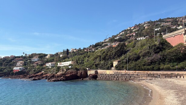 A coastal landscape with a clear beach, rocky shoreline, and hillside buildings. - Antheor Fairy Sea View 2 rooms in Villa (Saint-Raphaël)