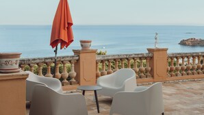 An outdoor seating area with two white chairs and an orange umbrella, overlooking a body of water and a rocky outcrop. - Antheor Fairy Sea View 2 rooms in Villa (Saint-Raphaël)