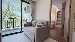 Ein modernes Wohnzimmer mit einer Couch, einem Balkon mit Blick auf Bäume und einem begehbaren Kleiderschrank.