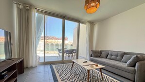 Uma sala de estar moderna com sofá, televisão, tapete estampado e varanda com vista.