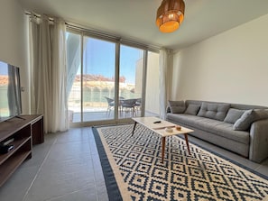 Una sala de estar moderna con un sofá, un televisor, un tapete estampado y un balcón con vistas.