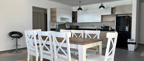 A modern kitchen with white cabinets, a black refrigerator, and a dining area with white chairs and a wooden table.