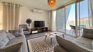 Uma sala de estar moderna com um sofá, uma TV, um ventilador e uma grande porta de vidro deslizante que dá para uma varanda.