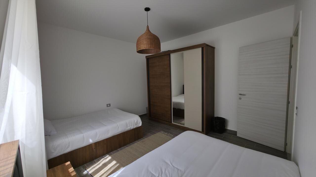 Ein Schlafzimmer mit zwei Betten, einem Kleiderschrank, einem Spiegel und einer Hängelampe.