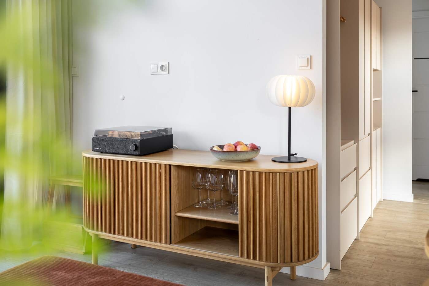 Quarto moderno com mesa de console de madeira, uma tigela de frutas, luminária e sistema de som.