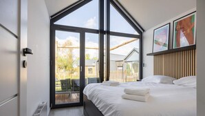 Ein Schlafzimmer mit großem Fenster, einem Bett, einem Holz-Kopfteil und Blick ins Freie.