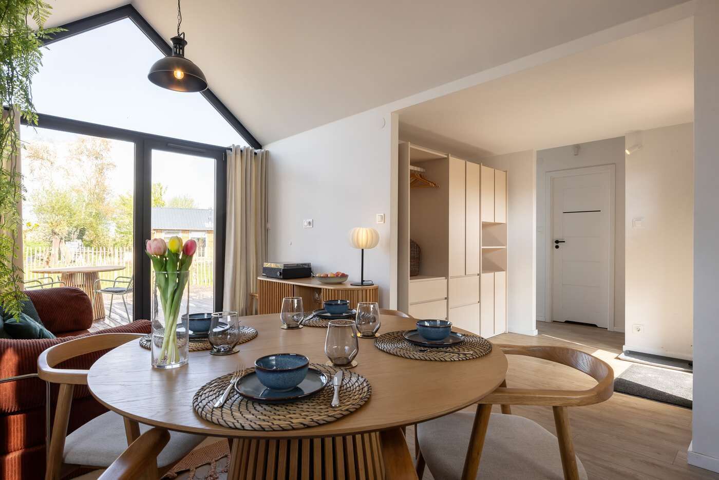 A dining area with a round table, chairs, and a vase of tulips.