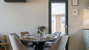 A dining area with a round table, grey upholstered chairs, and a view through a glass door. - Tiny house in Oud Ade | Tuin van Keet - 15 (Oud Ade)