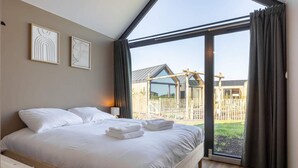 A bedroom with a large bed, a view of a wooden structure outside, and two framed artworks on the wall. - Tiny house in Oud Ade | Tuin van Keet - 15 (Oud Ade)