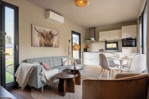 Ein modernes Wohnzimmer mit einer Couch, einem Esstisch mit Stühlen, einer Küchenzeile mit Schränken und Geräten sowie einem großen Fenster.