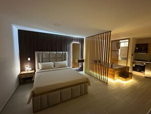 A modern bedroom with a large bed, bedside tables, a built-in bench, and a kitchen area with a stove. - Apartamento con Jacuzzi Parque Guatape Antioquia (Guatape)