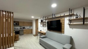 A modern living room with a grey sofa, a TV, and a wooden dining area. - Apartamento con Jacuzzi Parque Guatape Antioquia (Guatape)