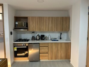 Een kleine keuken met ingebouwde apparaten, een magnetron, een fornuis, een koffiezetapparaat en een spoelbak.