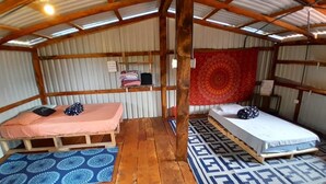 A compact room with two beds, a wooden floor, and a red tapestry. - Hippie Hut, Yoga and Relaxation (Paraiso)