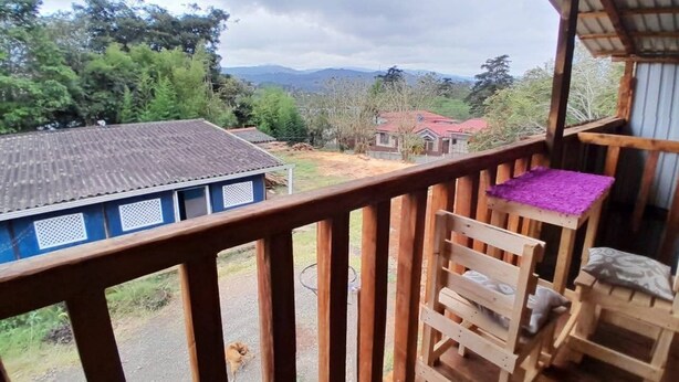 A balcony with a view of a rural landscape, a blue building, and a wooden deck. - Hippie Hut, Yoga and Relaxation (Paraiso)
