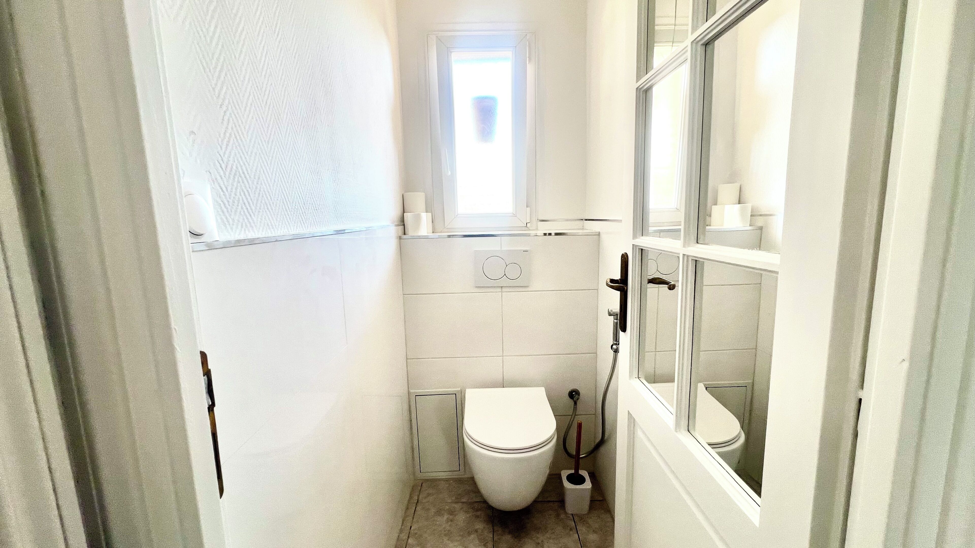 A small, white bathroom with a toilet, a window, and a shower.