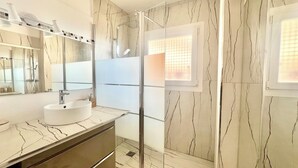 Ein Badezimmer mit weißem Waschbecken, einem Spiegel, einer Dusche und einem Fenster mit Blick.