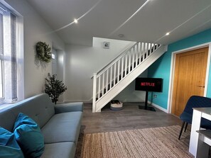 Ein Wohnzimmer mit grauem Sofa, einer Treppe, einem Fernseher und einer Holztür.