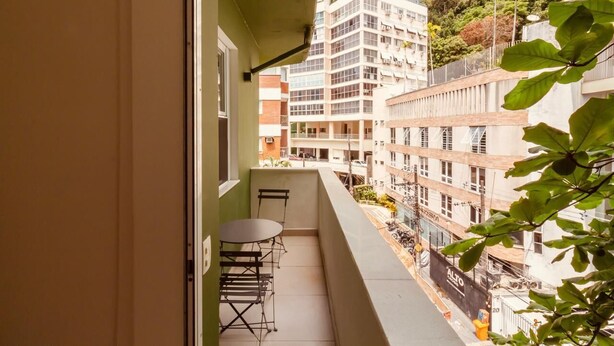 A balcony with a table and chairs, overlooking a cityscape with multi-story buildings and a hillside. - adv010 (Rio de Janeiro)
