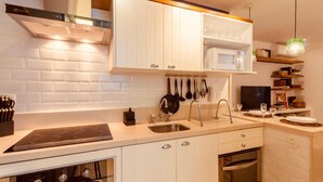 A modern kitchen with white cabinetry, a built-in microwave, a stove, and a hanging pot rack. - adv010 (Rio de Janeiro)