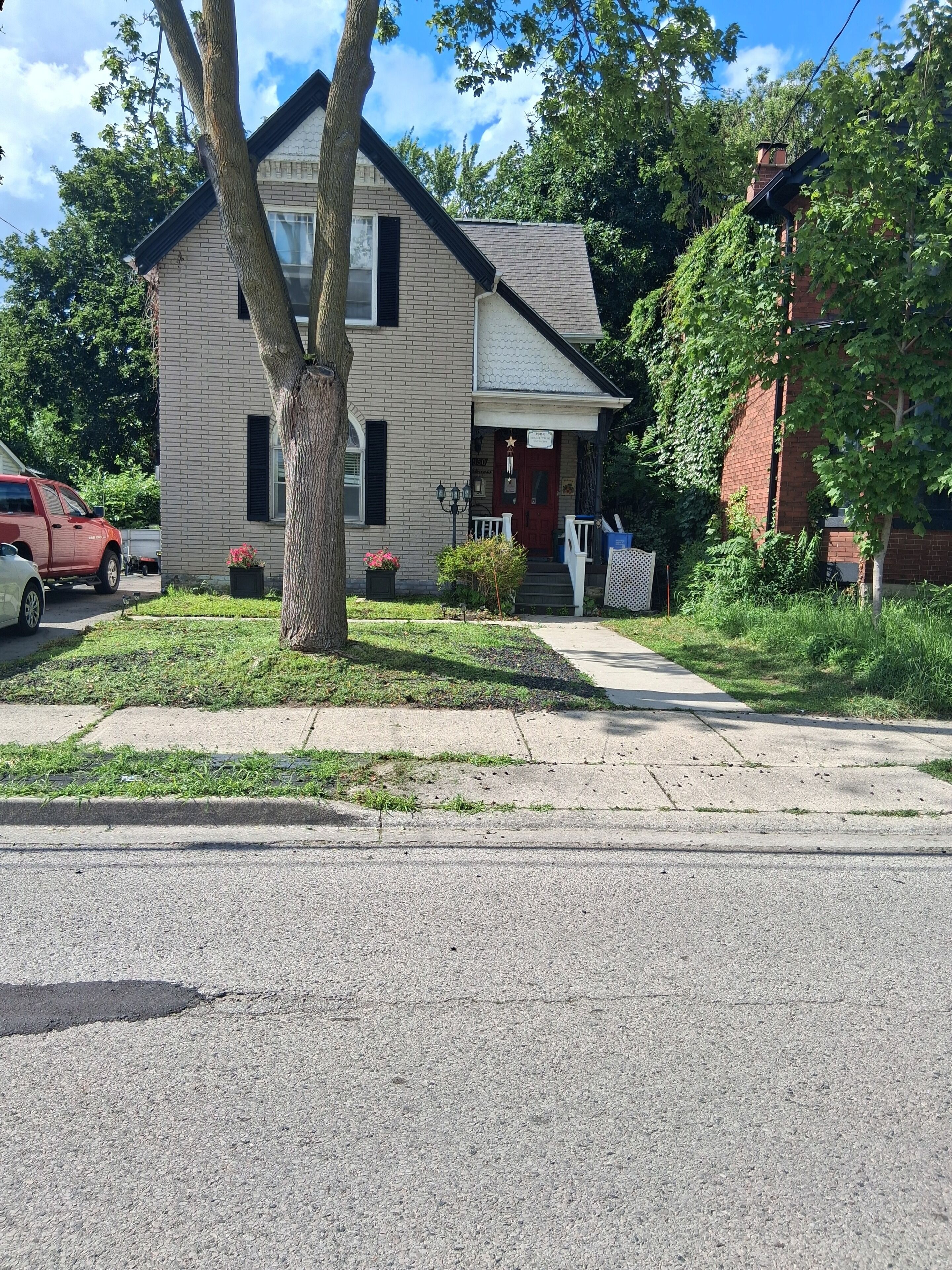 A two-story house with a front porch, a red door, and a small front yard.