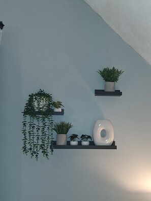 Una pared con tres estantes que sostienen plantas en macetas y un jarrón blanco.