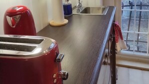 A kitchen with a red toaster, a sink, and a window with a view of trees and a house.