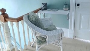 A wicker chair with a fluffy pillow, a white door, a white railing, and a framed picture on the wall.