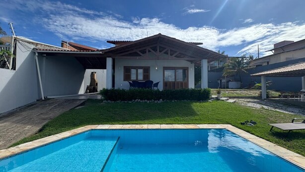 Ein Wohnhaus mit Swimmingpool, überdachter Terrasse und gepflegtem Rasen.