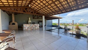 Eine Außenpatio mit einem Backofen aus Ziegeln, Fliesenböden, Korbstühlen, einer barrierefreien Bar und Blick auf die Stadt.