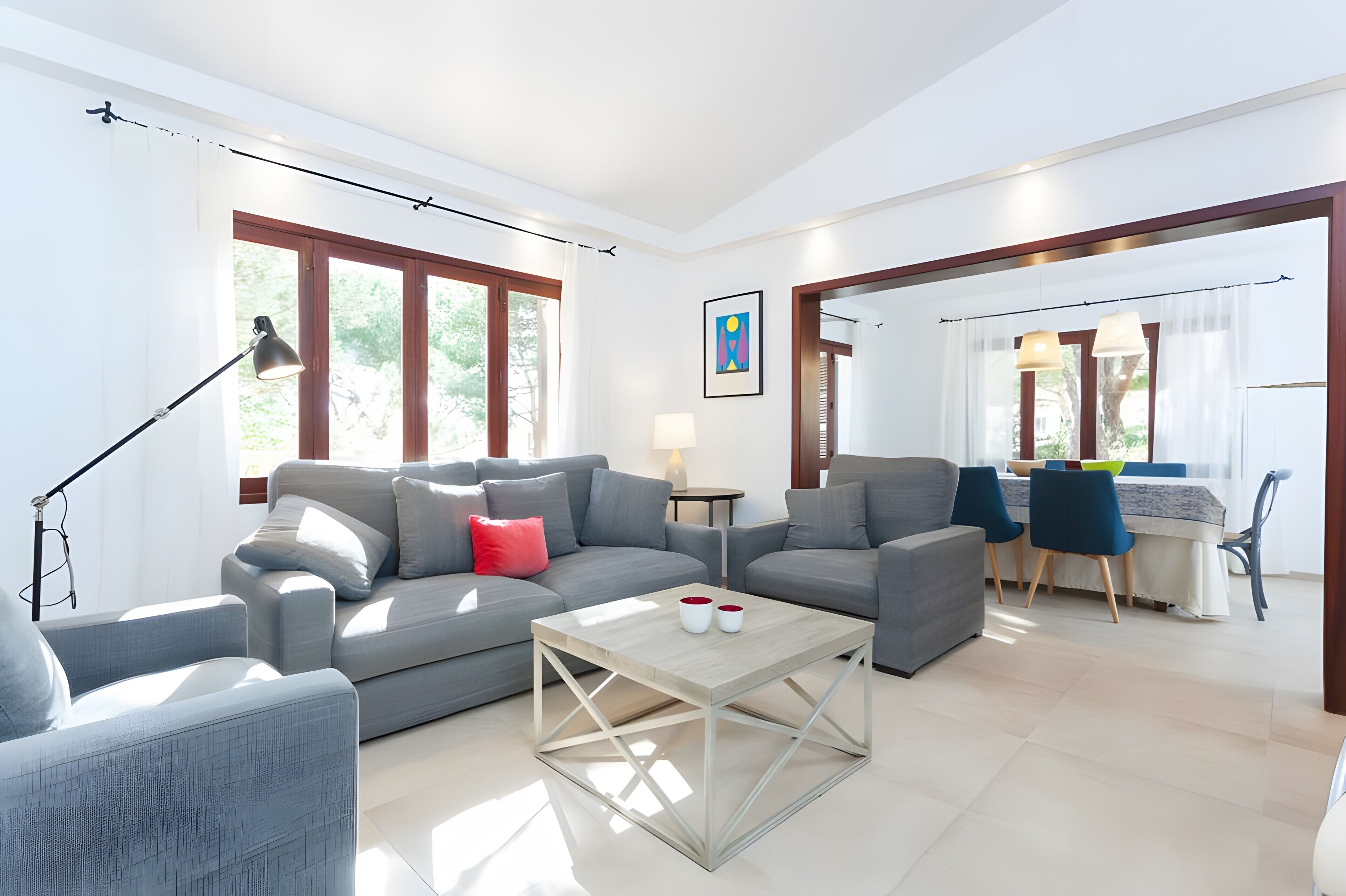 A modern living room with a grey sofa, a coffee table, and a dining area with a table and chairs.