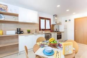 Eine moderne Küche mit weißen Schränken, einer Holz Arbeitsplatte und einem Essbereich mit Tisch für zwei Personen.