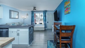 Una cucina moderna con zona pranzo, un'ampia finestra con tende, una ventola a soffitto e un televisore fissato al muro.