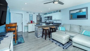 Eine moderne Küche mit einer zentralen Kochinsel, einem Essbereich mit Stühlen, einer Couch mit Kissen und einem Deckenventilator.