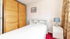 A bedroom with a wooden wardrobe, a white bed, a bedside table with a lamp, and a patterned curtain. - 2 Bed Flat - Sleeps 3 - Pets - Parking - Wifi (Oxford)