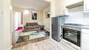 A modern kitchen with a gas stove, oven, and refrigerator. There is a sofa and a colorful rug in the living area. - 2 Bed Flat - Sleeps 3 - Pets - Parking - Wifi (Oxford)